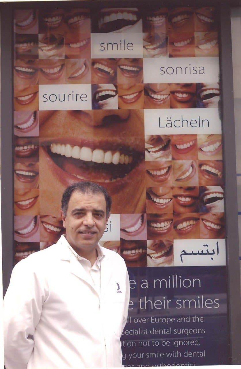 Professor Ameed Khalid Abdul-Hamid in a white clinical coat in front of a multilingual “smile” poster
